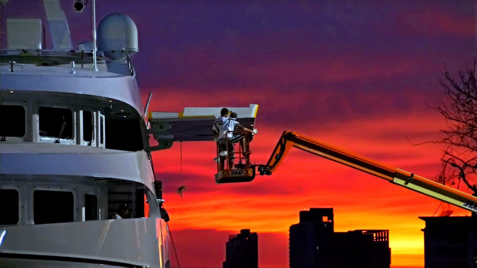 Boom-lift access for finishing a superyacht hull during a full Alexseal refair and repaint in Bangkok at sunset
